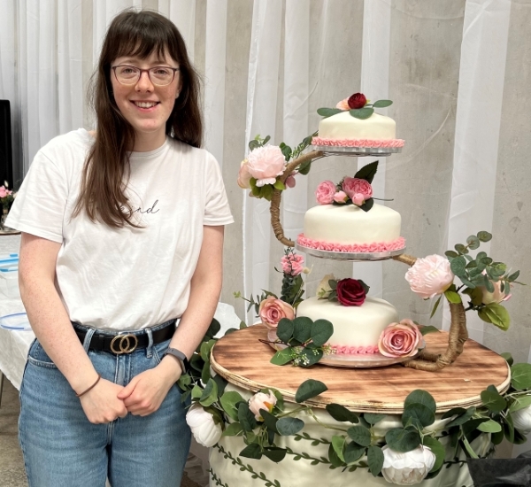 Alice Mainland standing in front of a three tiered cake Alice Mainland standing in front of a three tiered cake