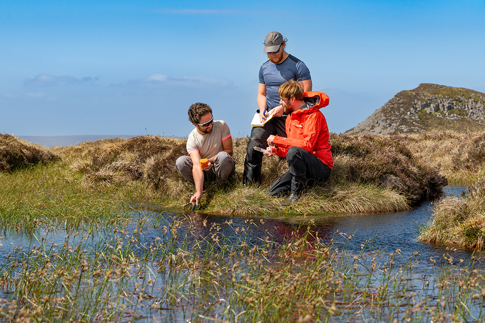 Three people taking a water sample in a peat bog Three people taking a water sample in a peat bog