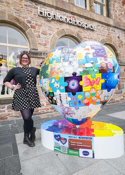 Antonia Pritchard, Associate Professor at UHI, standing with HeART 5: Sonder artwork outside the Highland Hospice shop on Falcon Square, Inverness. Photo credit: UHI and Paul Campbell.