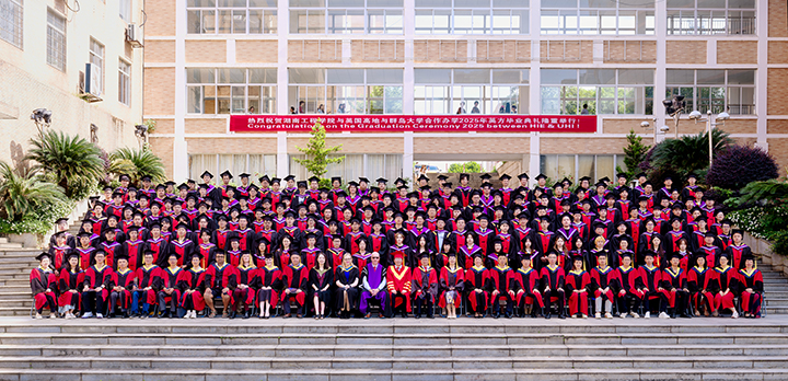 A group of students graduating wearing formal graduation robes sitting for a posed photo outside a university building