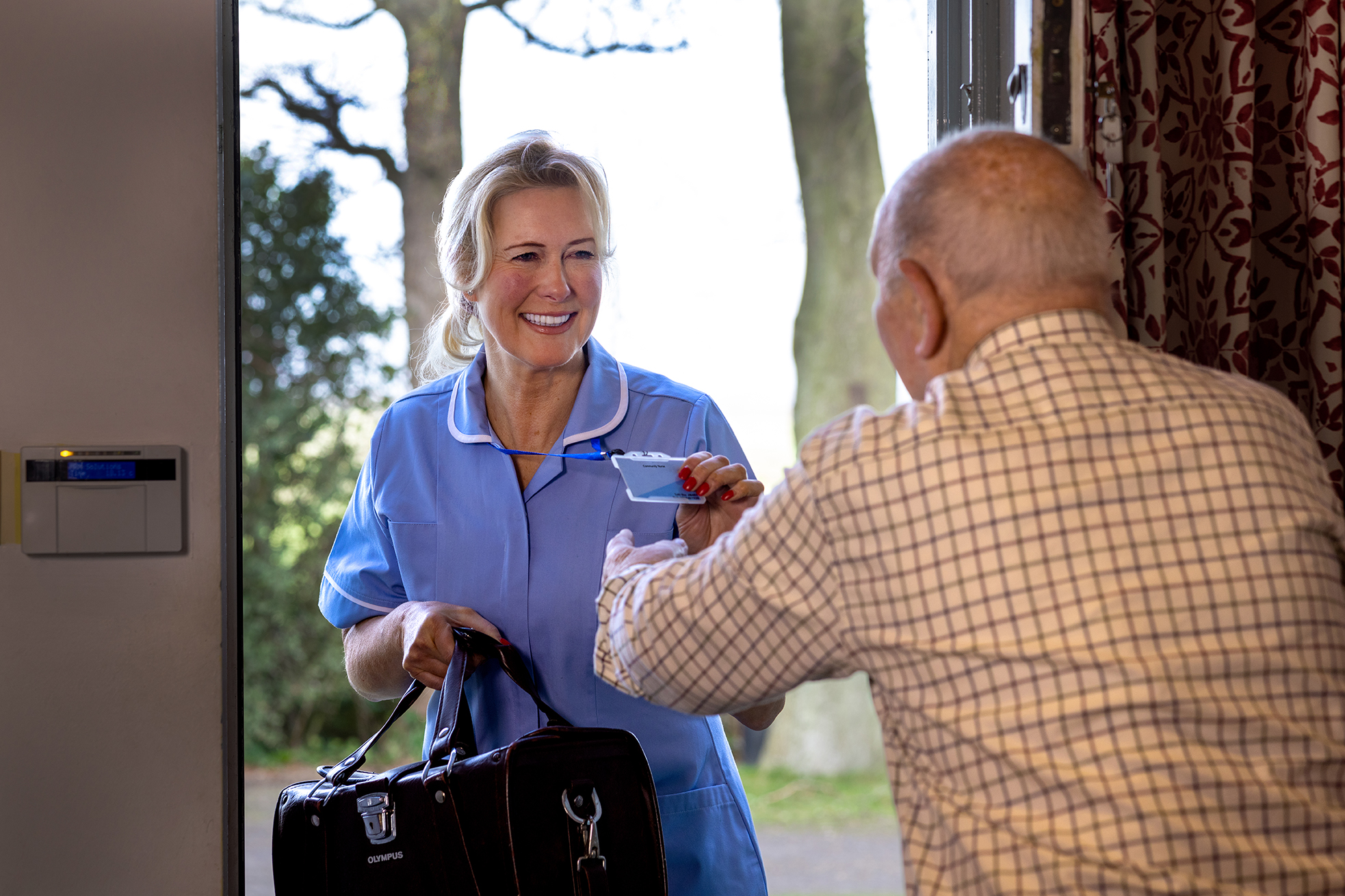 A nurse being greeted by an elderly man at a front door A nurse being greeted by an elderly man at a front door